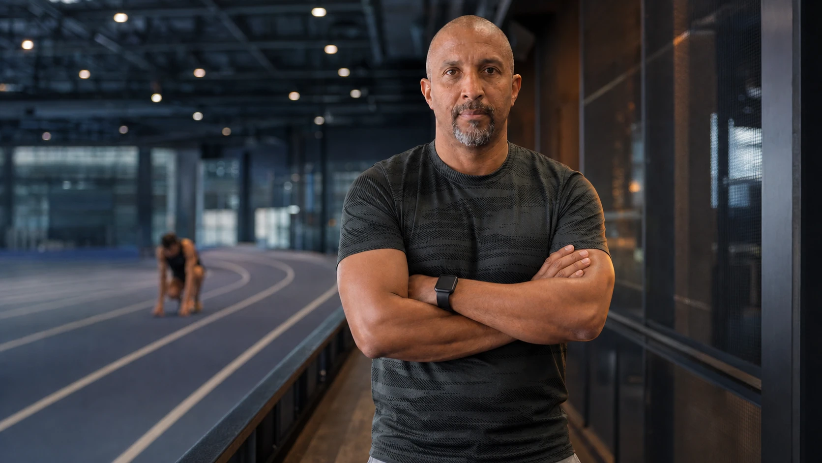 A mental performance leader beside an indoor track as an athlete prepares in the distance